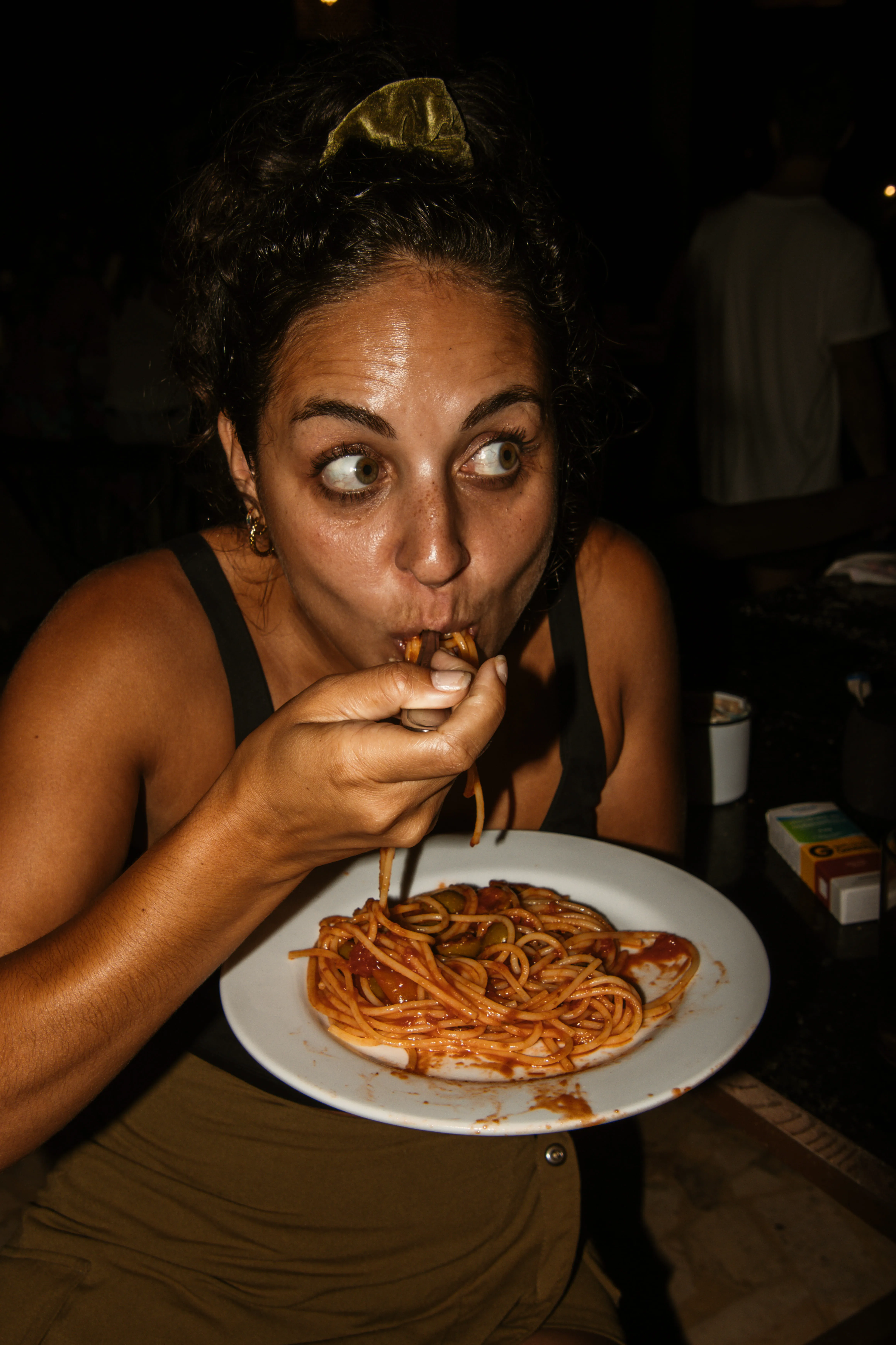 Woman with curly hair tied back eating spaghetti with tomato sauce from a white plate.