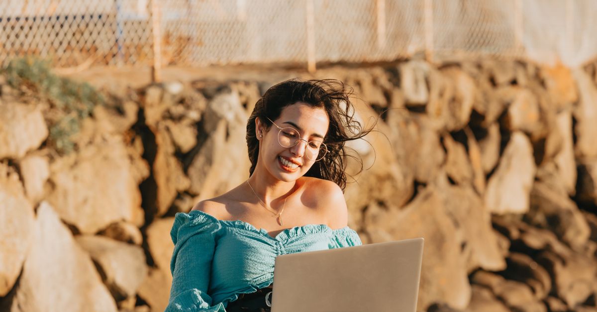 Digital nomad smiling while working on a laptop outdoors